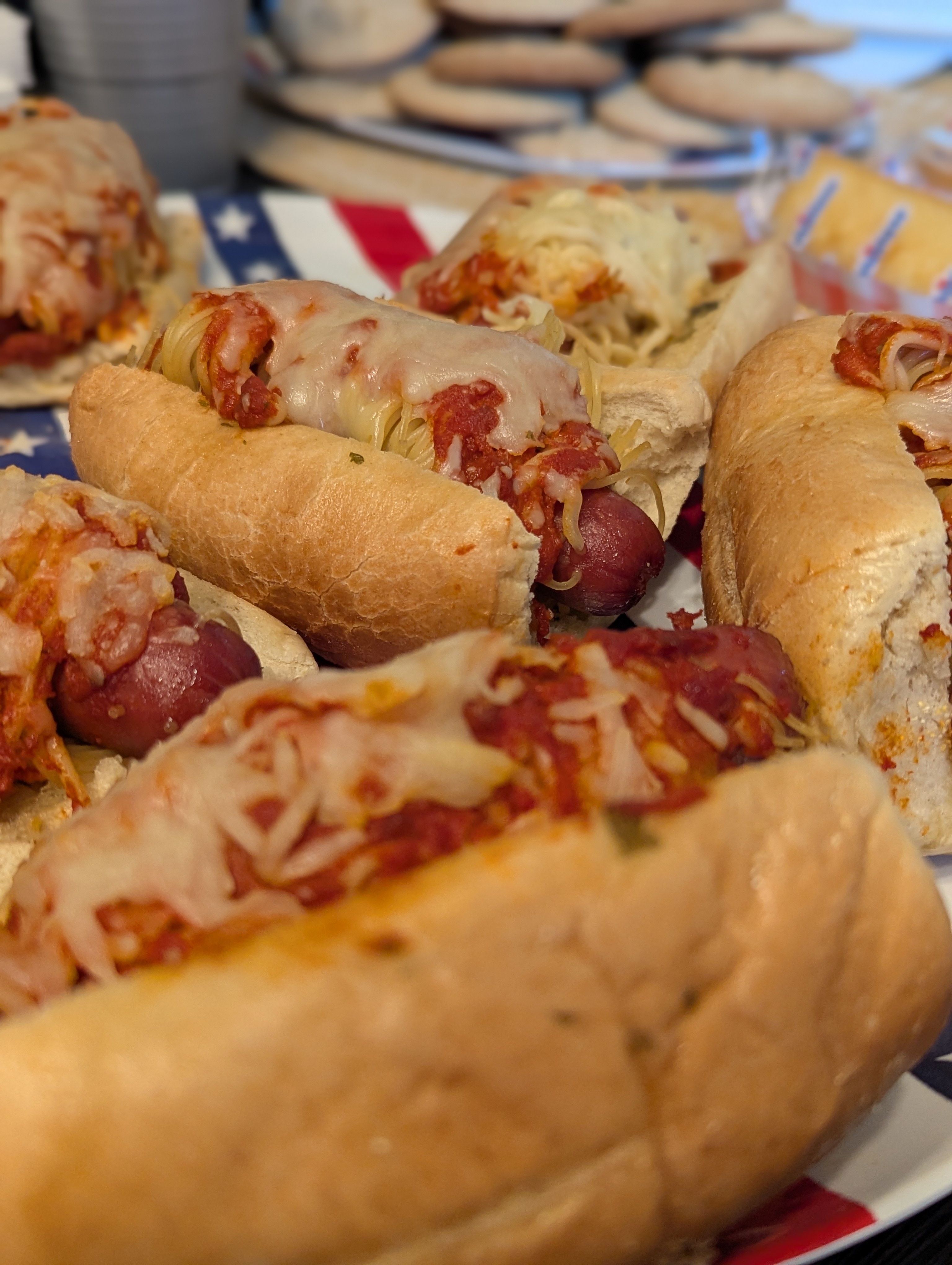 Half a dozen hotdogs, covered in spaghettis and red meat sauce, served in garlic bread buns