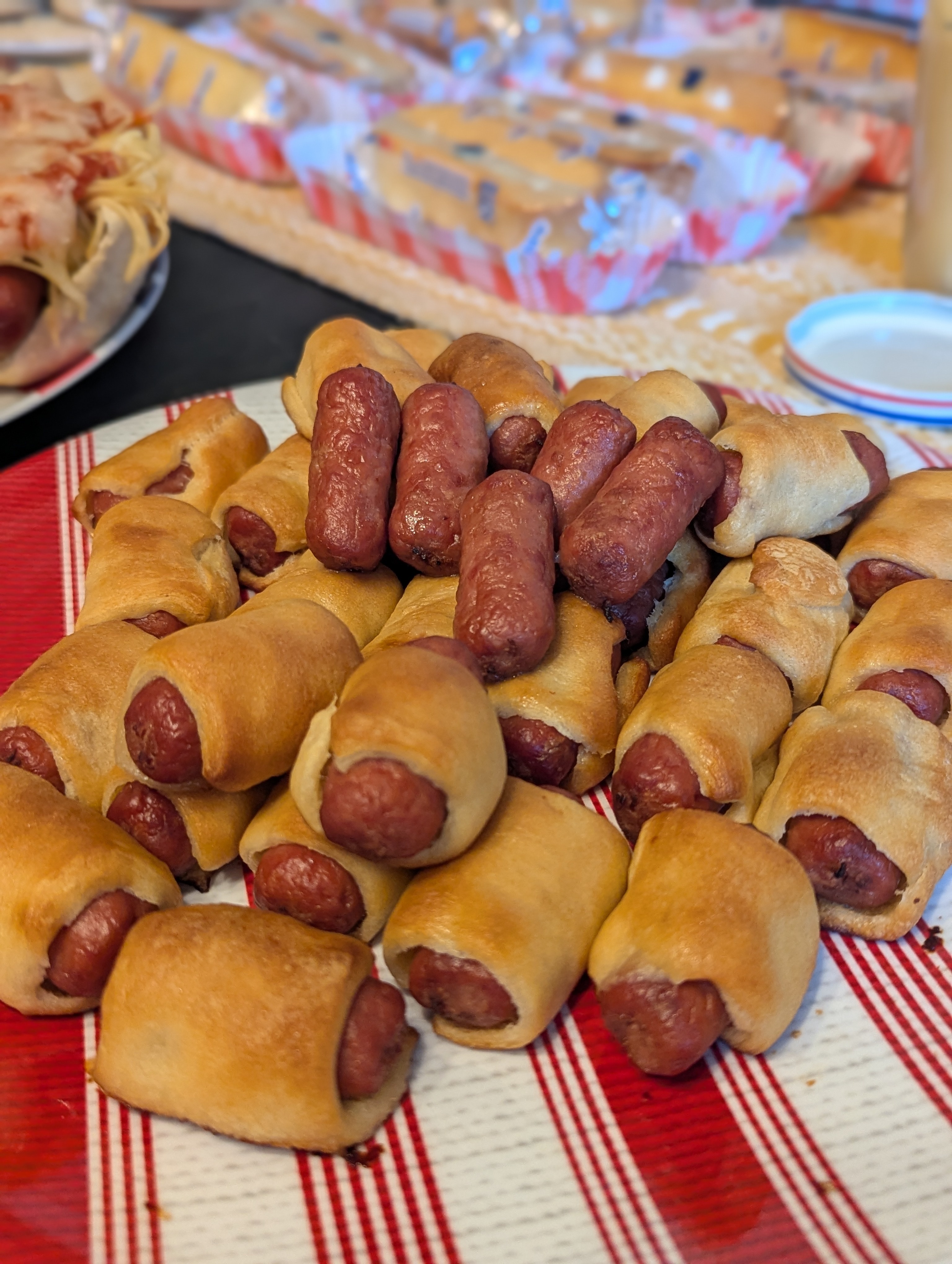 A plate of basic hotdog weenies, some wrapped in puff pastry. In the background of this image, you can see evidence of true depravity: Twinkies placed in paper sleeves, lined up and prepared to serve as buns for hotdogs.
